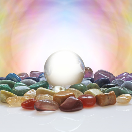A clear, round, crystal ball sits in the middle of colorful gemstones.