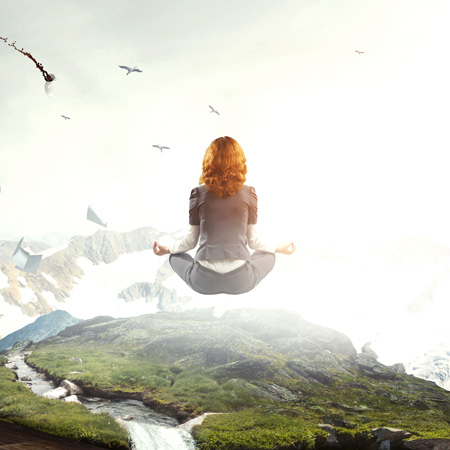 A woman meditating while floating high above the grassy ground. Birds fly around her.