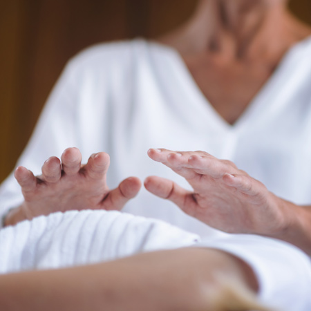 A woman performs reiki therapy by holding her hands over another person's body.